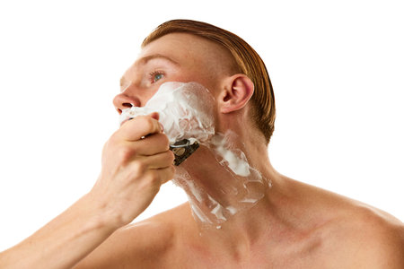 Facial grooming. Serious male model, attractive guy shaving with razor against white studio background. Concept of natural beauty, selfcare, body and skincare, hygiene treatments, fashion.の写真素材