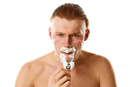 Facial grooming. Serious male model, attractive guy shaving his beard with razor against white...