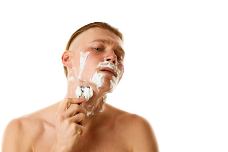 Hygiene treatments. Attractive man shaving beard with shaving foam looking at camera against white studio background. Concept of natural beauty, selfcare, hygiene, facial grooming, barber. Copy space.の写真素材
