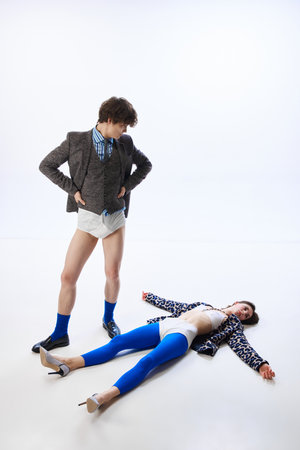Young man in suit but without pants, in underwear, looks in bewilderment at girl who strangely and brightly dressed lying on floor. Concept of romance, bizarre love, Valentine Day, fashion, glamourの写真素材