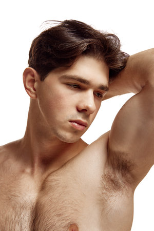 Close up portrait of attractive brutal young man with bare shoulders put his hand behind his head against white studio background. Concept of natural beauty, body care, male health, masculinity,の写真素材