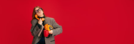Tired young lady holding the receiver of dead old landline phone against vivid red studio background with negative space for your text. Concept of business communication, study and knowledge.の写真素材