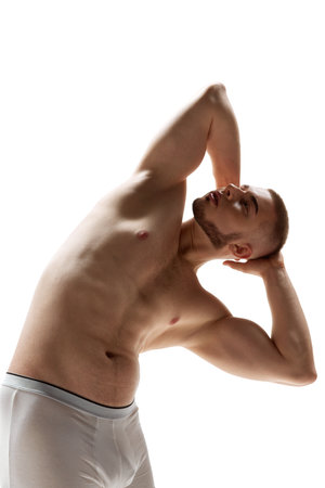 Young handsome man with athletic body shapes put his hands behind his head and bent over against pristine white background. Concept of male health, natural beauty people, self care. Copy space.の写真素材