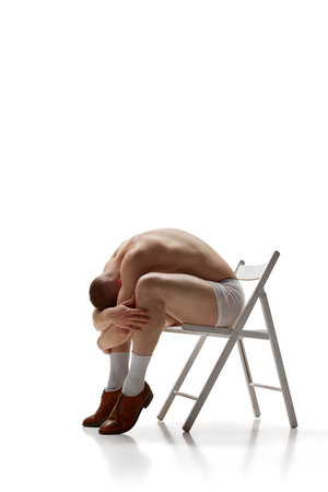 Naked man in underwear sits on chair with his head on his knees and his arms over his head against white background. Concept of mens health, beauty, body and skin care, fitness. Body artの写真素材