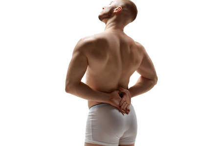 Rear view photo of naked athletic young man showing muscles of back and hands against white studio...
