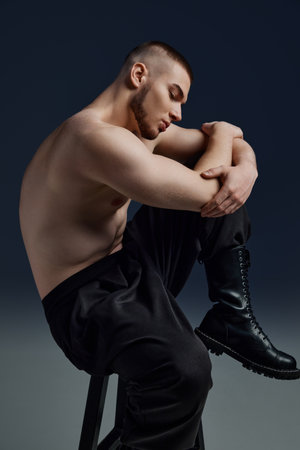 Side view portrait of young handsome bristled man with naked torso sitting on chair showing his muscled body. Concept of mens health, beauty, body and skin care, fitness. Body artの写真素材