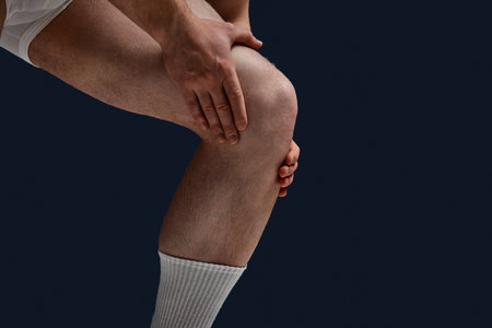 Cropped close up photo of female lag. Man put hand on knee because he feel pain, joints hurt against blue studio background. Concept of mens health, lifestyle, beauty, body and skin careの写真素材