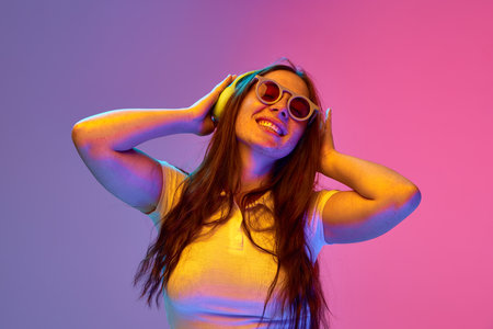 Positive, overjoyed girl, student singing and dancing while listening music in headphones against...