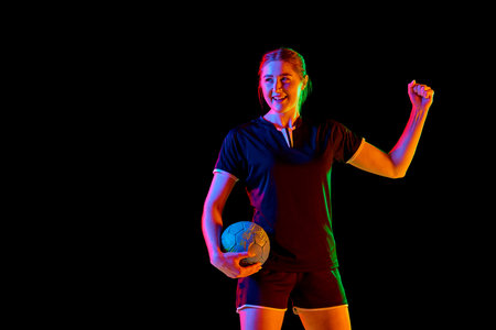 Young woman, professional handball athlete happy because she scored perfect decisive goal against black background in mixed neon light. Concept of professional sport, championship 2024, victory. Adの写真素材