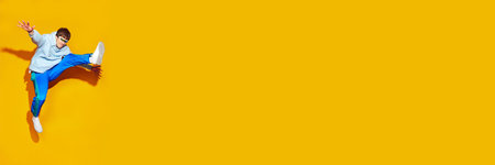 Young attractive man, dressed in comfy sportwear jumping in motion against vivid yellow background...