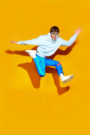 Dynamic fashion moment as young man leaps in modern, comfy attire against striking yellow...