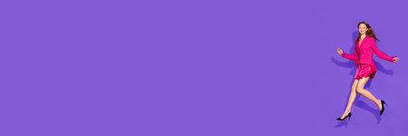 Trendy fashion in motion. Woman jumps with flair, dressed elegant suit, shows pop of excitement against bright purple background with negative space for text. Concept of beauty, shopping, sales. Adの写真素材