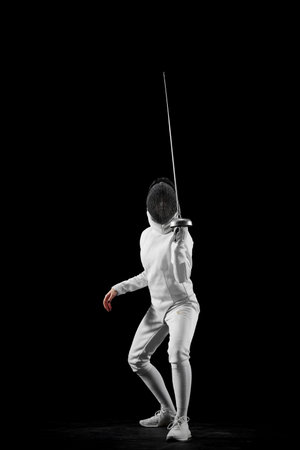 Swordswoman, professional female fencers poised stance, against black studio background. Intensity and excitement of fencing. Concept of professional sport, active and healthy lifestyle, championshipの写真素材
