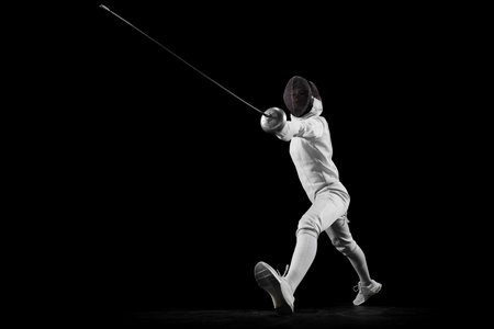 Dynamic portrait of female fencer training attack technique in motion. Swordswoman focused and determined, her eyes fixed on her opponent. Concept of professional sport, active lifestyle, championshipの写真素材