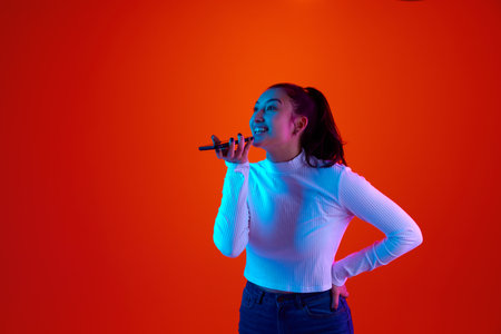 Portrait of beautiful young woman, student orders home delivery by phone against gradient orange-red background in neon light, filter. Concept of shopping, sales season, working online, delivery. Adの写真素材