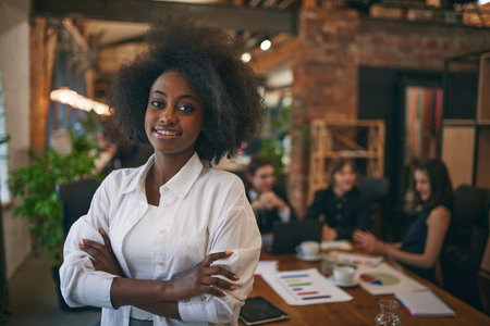 Portrait of African-American woman smiling at camera while classmates studying with laptop on background. Public library. Concept of study, co-working space, teamwork, collaboration, classmates.の写真素材