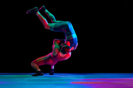 Two young man, professional sportsman of freestyle wrestling in uniform fighting against black...