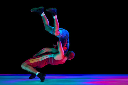 Dynamic shot of two professional Greco-Roman wrestlers in red and blue uniform wrestling against black background in mixed neon lights. Concept of motion, action, combat sports, strength and power.の写真素材
