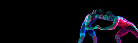 Banner. Two freestyle wrestlers hand fighting in mixed neon lights against black background with negative space to insert text. Concept of fair wrestling, championship, win competition.の写真素材