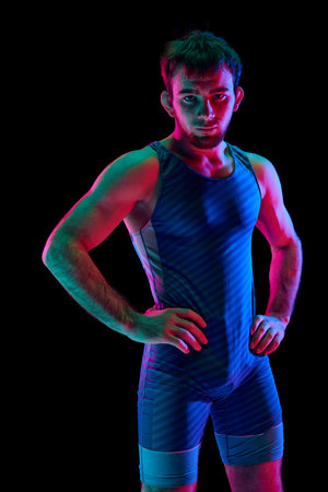 Focused and competitive freestyle wrestler in modern blue sportwear put his hands on hips and...