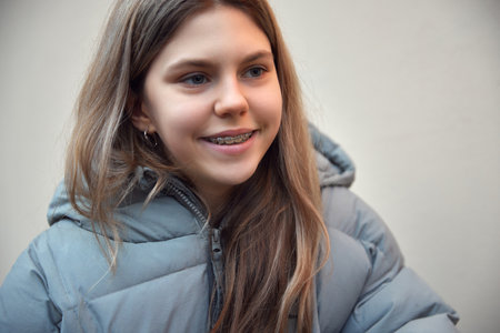 Close-up portrait of cute smiling teenage girl with braces wearing in warm coat looking away against...