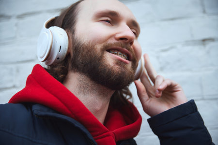 Close up portrait of joyful young man with dental braces smiling while listening music in headphones outside. Concept of health care and medicine, beauty, lifestyle, positive, leisure time. Adの写真素材