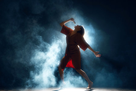 Voice Unbound. Solo artist performing live, arm extended, amidst atmospheric stage lighting and fog against black background. Concept of hobby, festival, concert, disco, entertainment. Adの写真素材