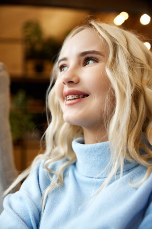 Joyful teen girl with dental braces, blonde curls, gazing upward in delight against blurred background. Selective focus. Concept of youth and healthcare, medicine and beauty, confidence and selfcare.の写真素材