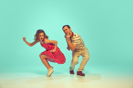 man and woman, talented dancers in retro style clothes dancing swing, boogie-woogie against gradient...