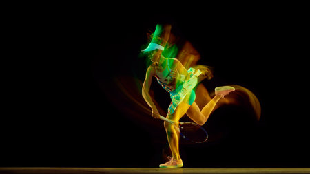 Dynamic photo of young sportive woman, tennis player in full match swing with motion blur against black studio background. Concept of women in sport, active lifestyles, energy, movement.の写真素材