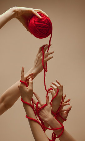 Friendship. Hand holds ball of threads and hands nearby unravel this tangle, intertwining and uniting against sandy color studio background. Concept of human touch, beauty and care, spa procedures.の写真素材