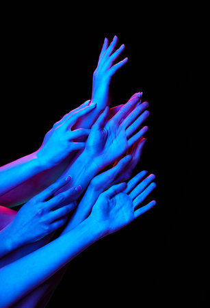 Group of hands reaching to something in multicolored neon lighting against black studio background. Unity and connection. Concept of human touch, beauty and care, spa procedures.の写真素材
