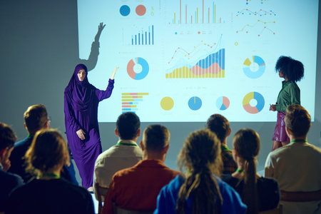 Speaker in hijab raising hand to emphasize point during presentation, with attendee walking to stage in conference room. Concept of business, startup, leadership and personal development courses.の写真素材