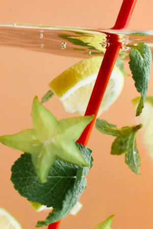 Slices of lemon and starfruit with mint leaves submerged in water with red straw. Refreshing...