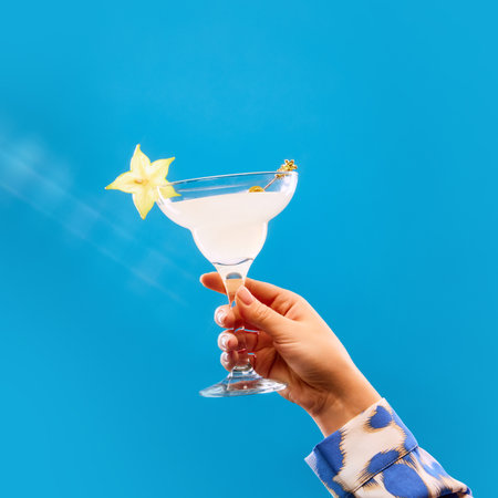 Unrecognizable woman holding glass of sweet and sour cocktail decorated with slice of carambola against blue studio background. Concept of alcohol, drink, party, degustation, holiday. Copy space. Adの写真素材