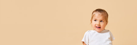 Banner. Portrait of cute, playful little girl looking away against beige studio background with...