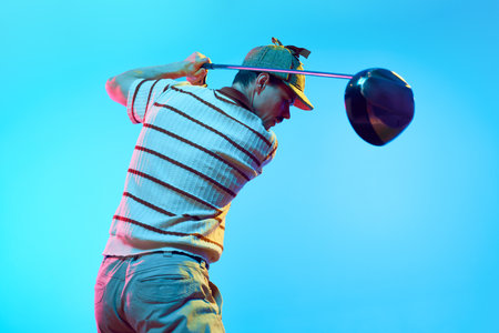 Rear view of man completing golf swing n mid follow-through with focus on club in neon light against gradient blue background. Concept of professional sport, luxury games, active lifestyle, action. Adの写真素材