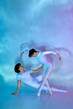 Contemporary ballet dancers in white attire performing artistic dance move in neon light against gradient studio background. Concept of beauty and elegance, dance grace, inspiration, creativity.の写真素材