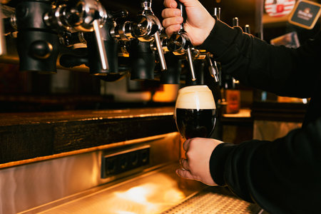 Close-up of hand filling pint glass from draught beer tap in pub. Cold refreshing dark beer poring to glass. Concept of alcohol drinks, nightlife, party, festivals, Oktoberfest. Adの写真素材
