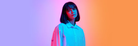 Banner. Young woman with calm expression looking at camera in neon light against gradient studio...