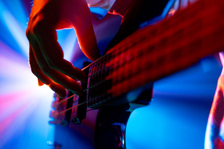 Guitarists hands plucking strings of bass, electric guitar with dynamic stage lighting on blurred...