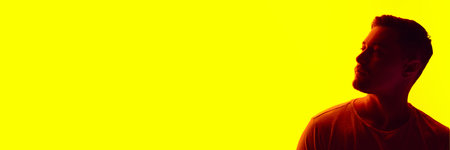 Banner. Silhouetted portrait of handsome man posing in red neon light against vibrant yellow studio...