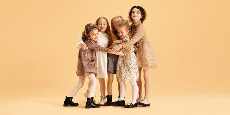 Cute, overjoyed little girls, kids stands in group and hugs dressed trendy, glamour outfits against...