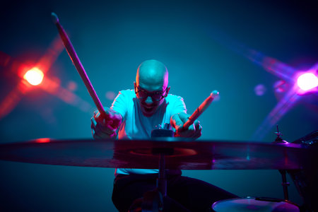 Emotional bald drummer in casual outfit with drumsticks in pink-purple stage lighting against gradient studio background. Concept of music and art, hobby, concerts and festivals, modern culture. Adの写真素材