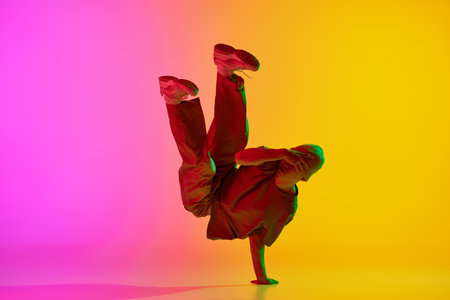 Artistic, young man, break-dancer dancing in motion in neon light against gradient pink-yellow background. Concept of hobby, sport, creativity, fashion and style, motion, action. Adの写真素材