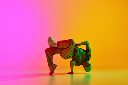 Young athlete man, dressed street style outfit dancing in motion in neon light against gradient...