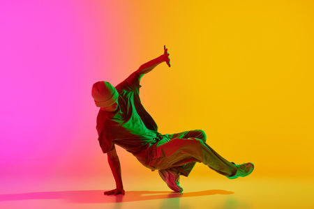 Talented dancer dressed streetwear performing freestyle moves in motion in neon light against gradient pink-yellow background. Concept of art, hobby, sport, creativity, fashion and style, action. Adの写真素材