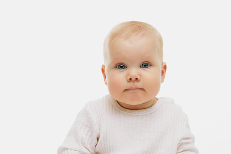 Portrait of cute, charming little baby, kid in dressed in white clothes looking at camera against...