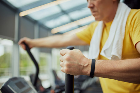 Cropped photo of senior man in vibrant sports attire with towel on shoulders training on exercise machine modern gym. Concept of sport, active seniors in modern life, healthy lifestyle. Adの写真素材
