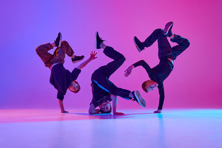 Energetic photo of talented boys, in black attire performing hip-hop in motion in mixed neo n light against vibrant gradient background. Concept of sport and hobby, music, fashion and art, movement.の写真素材
